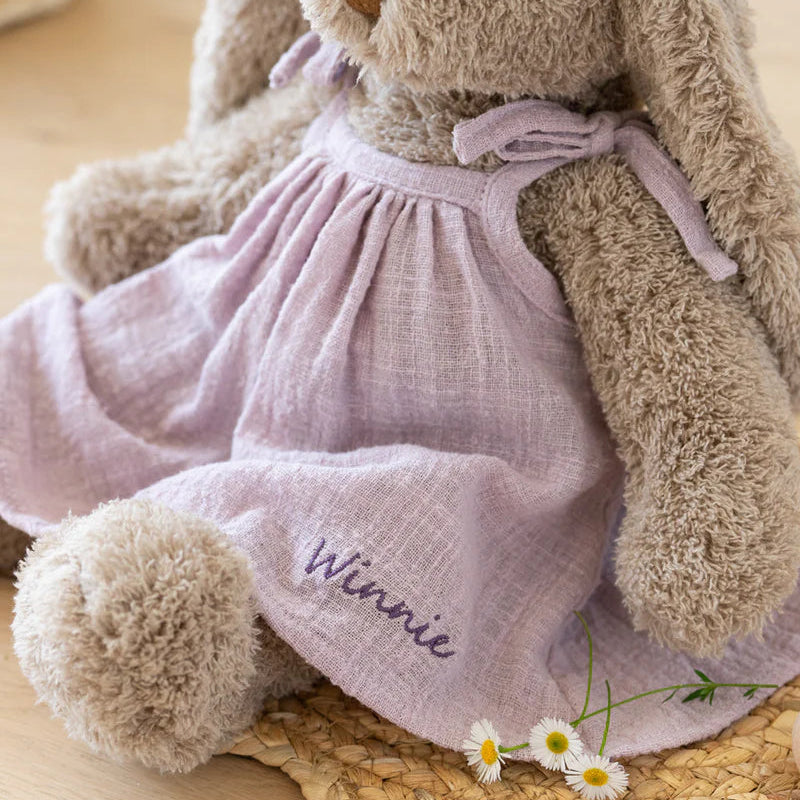 Teddy bear in a pink dress with 'Winnie' on a wooden surface