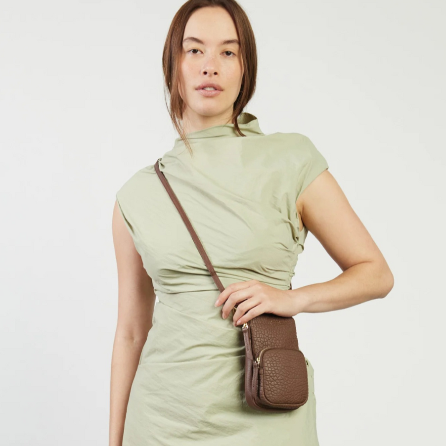 Woman wearing a light green dress holding a brown crossbody bag on a white background