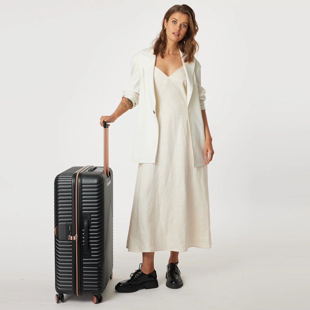 Woman in a white dress standing next to a black suitcase on a white background