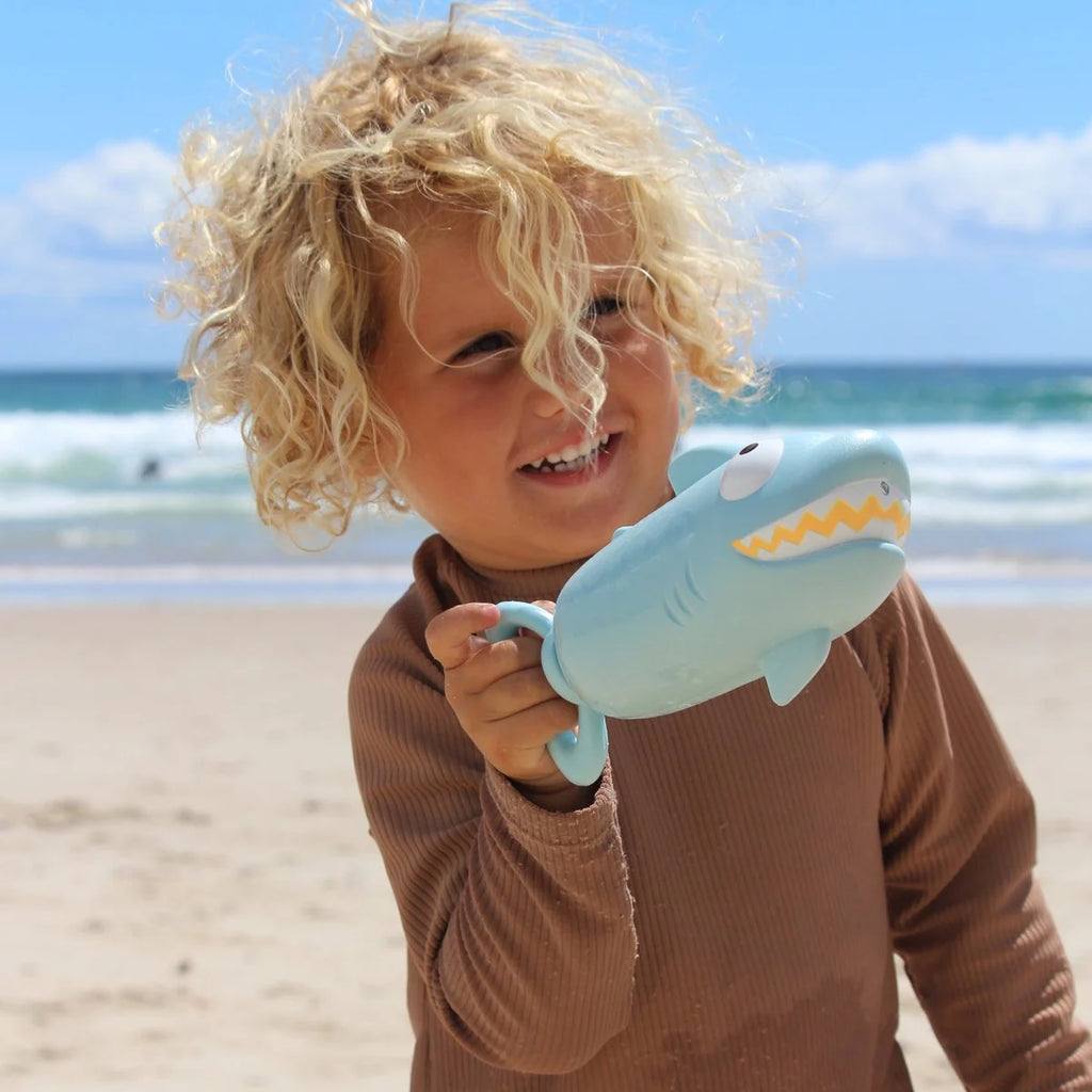 Child holding a shark toy on a beach