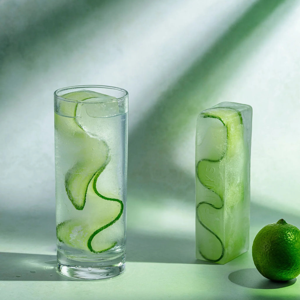 Glass of cucumber water with a lime on a light background