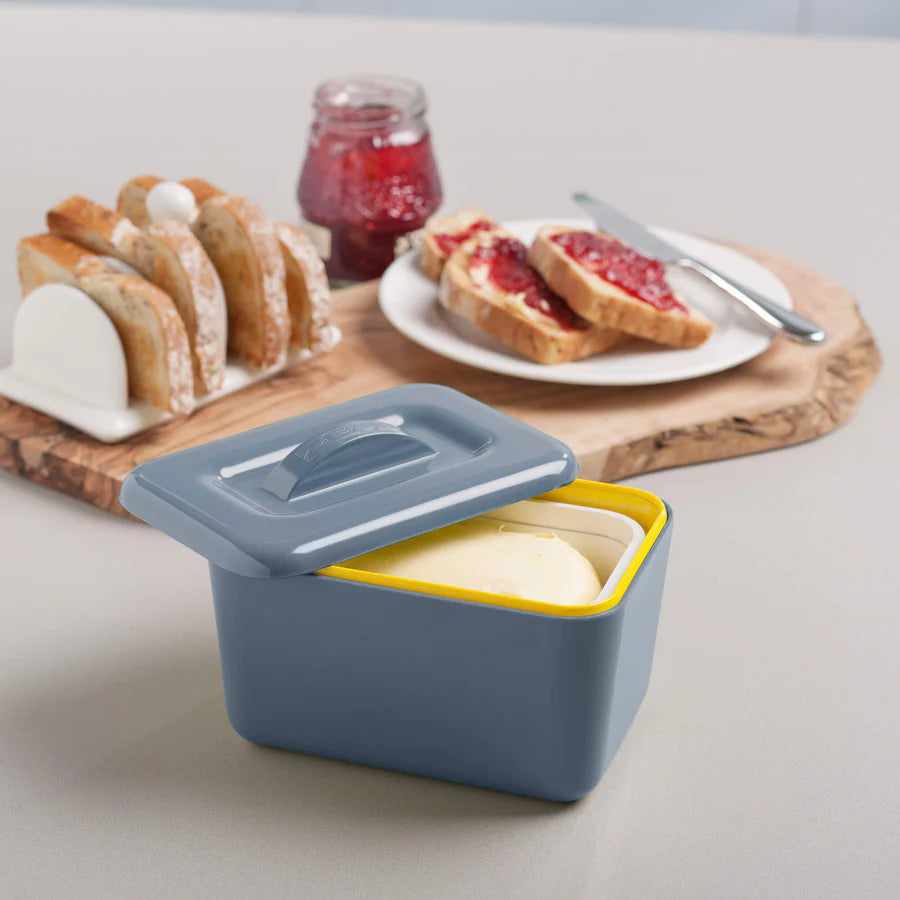 Butter container with a yellow interior on a table with toast and jam in the background