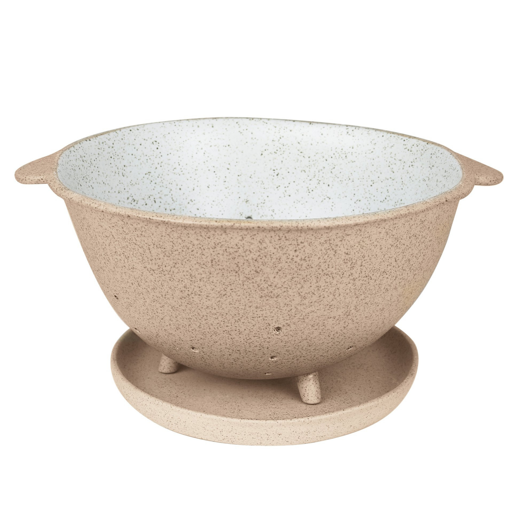 A ceramic colander on a plate made of a beige and black speckled clay with a white and black specked glaze on the inner bowl