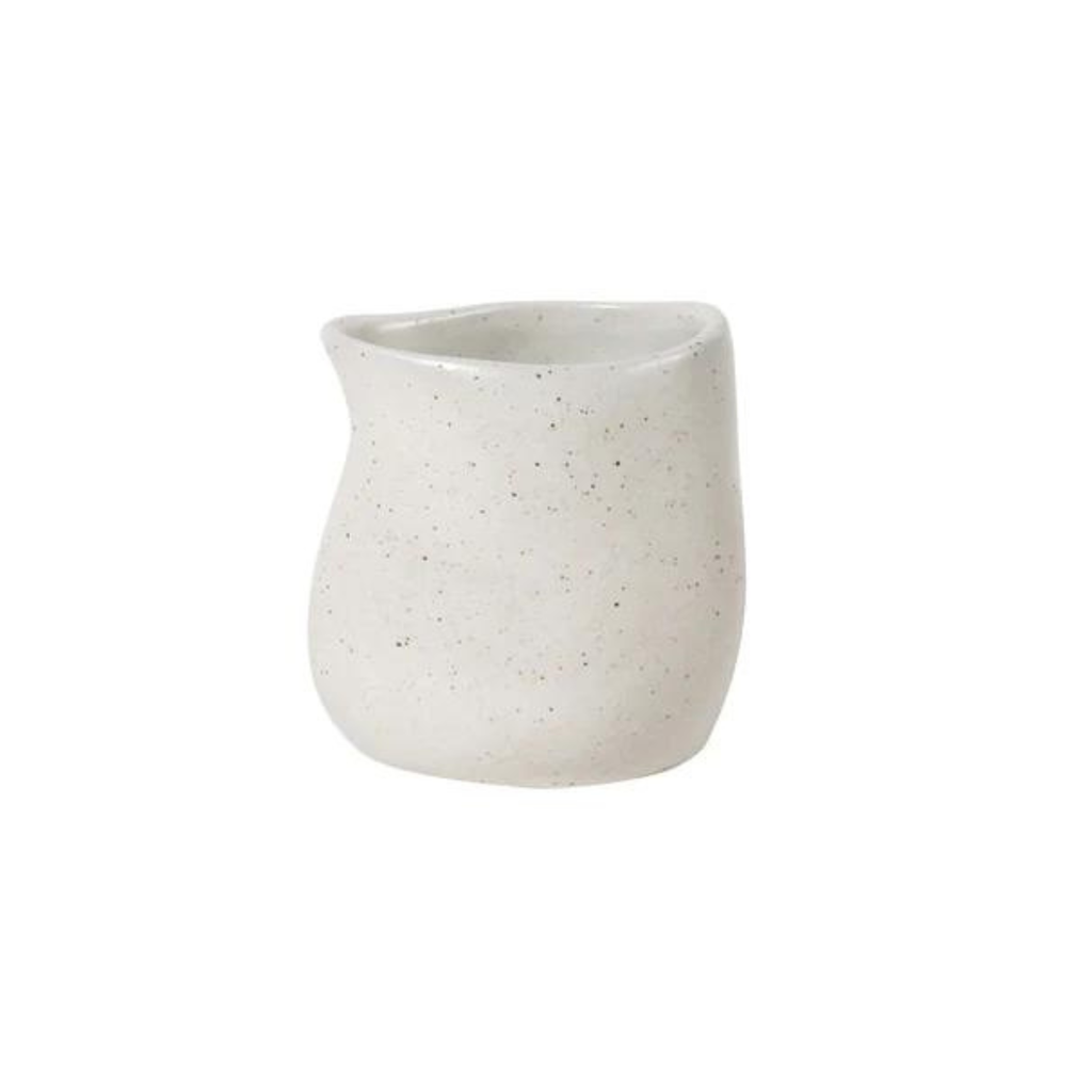 A ceramic white small pouring jug with black speckles against a white background 